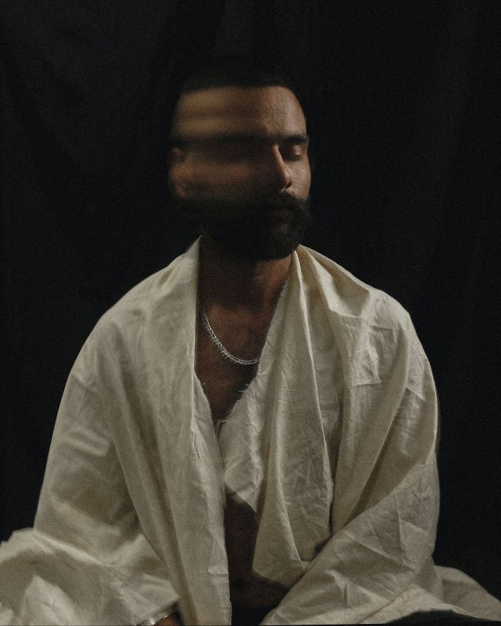 Long exposure of Asian male living with psychological disorder in white worn out robe sitting on floor and moving head against black background